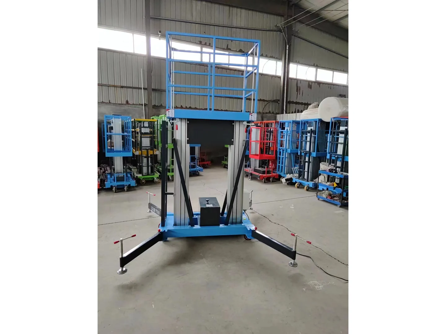 Complete blue double mast lift lowered with its stabilizers deployed among other equipment