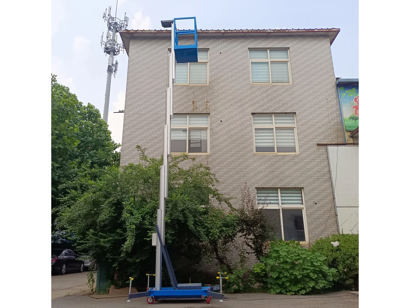 Complete blue single mast lift raised with its platform, mast, wheels and stabilizers visible