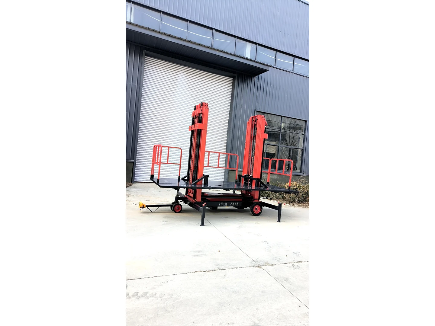 Complete red twin-mast electric scaffold with platform, tow bar, wheels and stabilizers outside a building