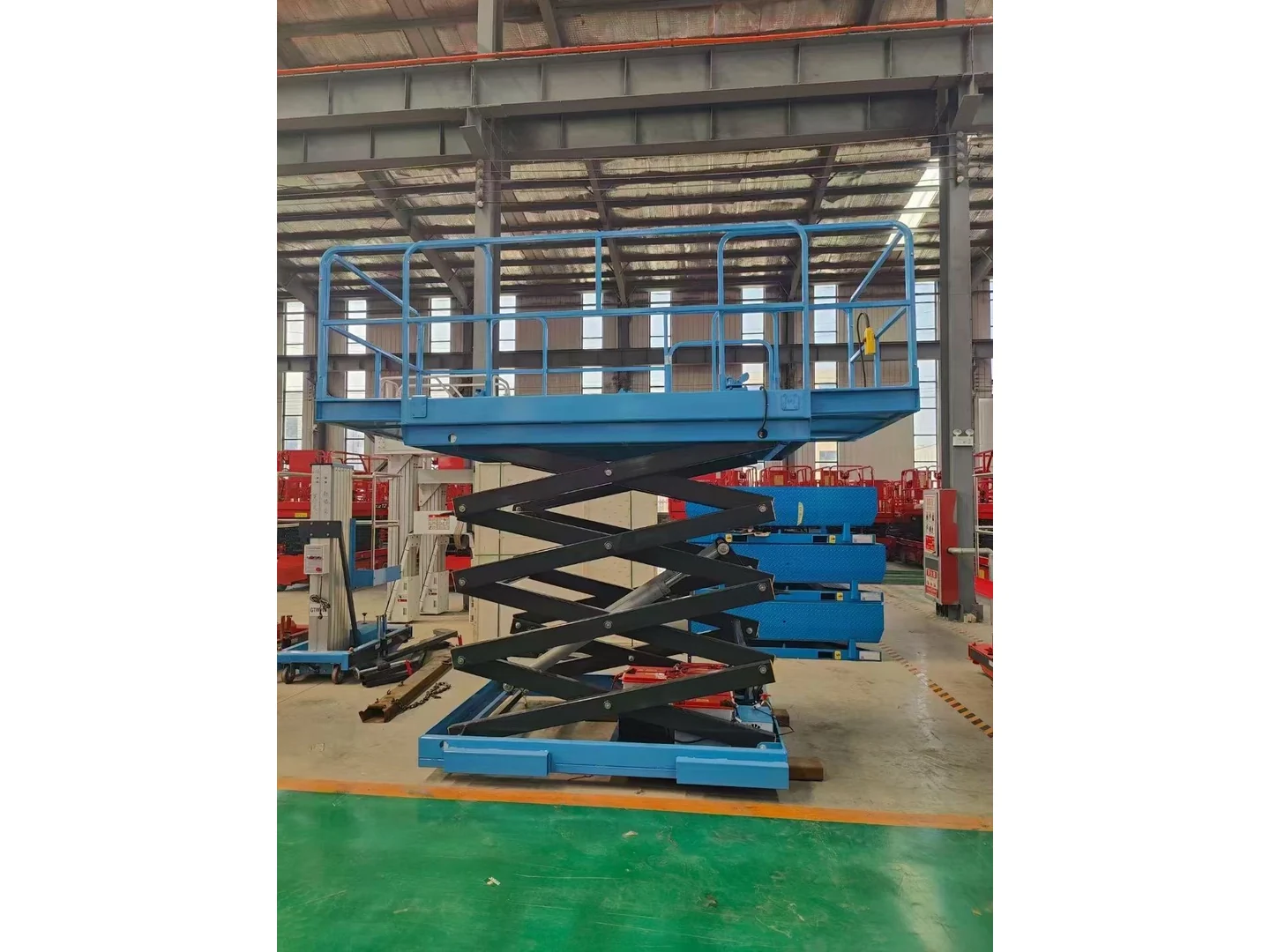 Raised blue fixed scissor lift table with guardrails and a complete base in a workshop