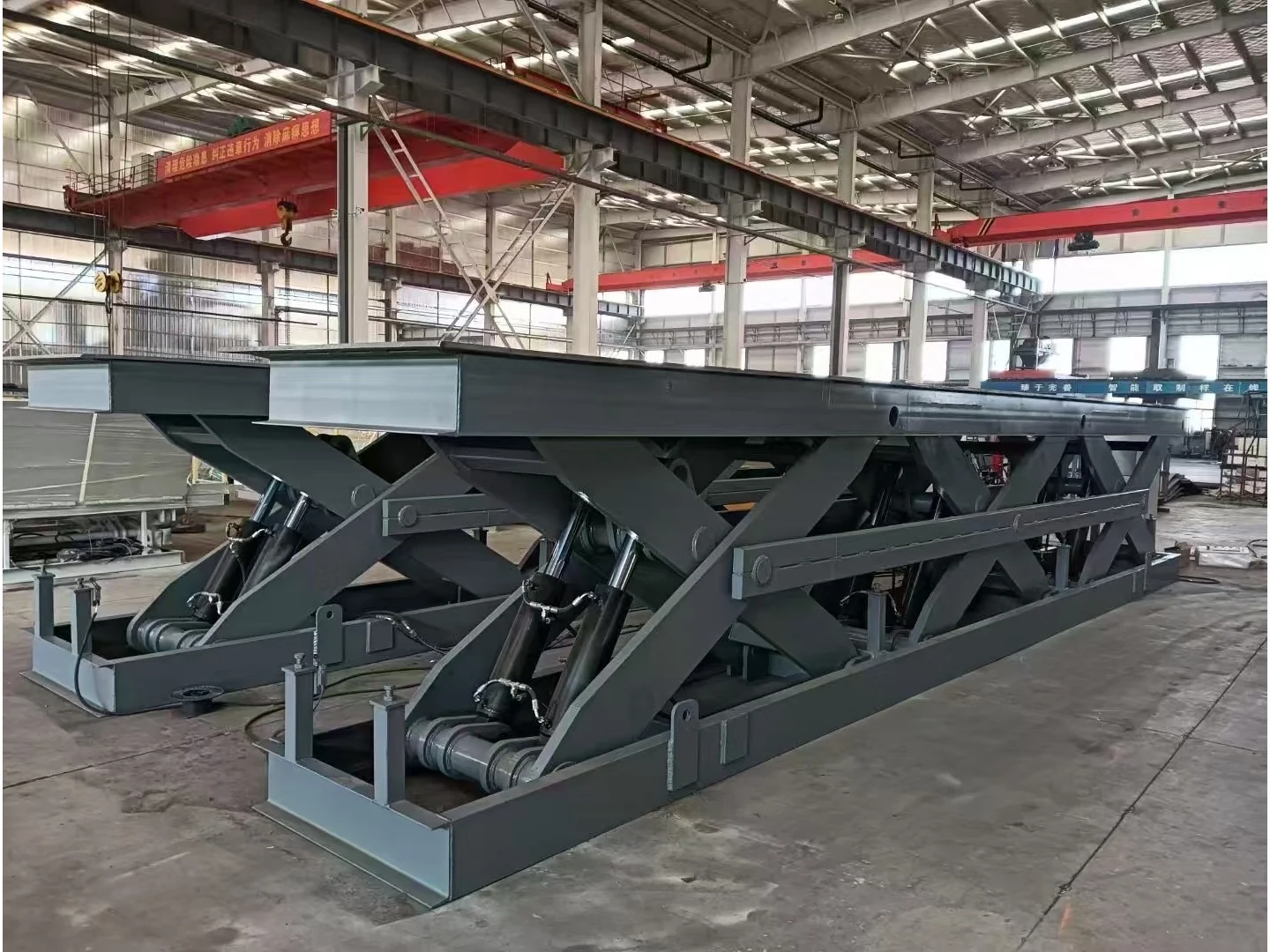 Gray fixed scissor lift table showing its full platform, hydraulic cylinders and base in a workshop
