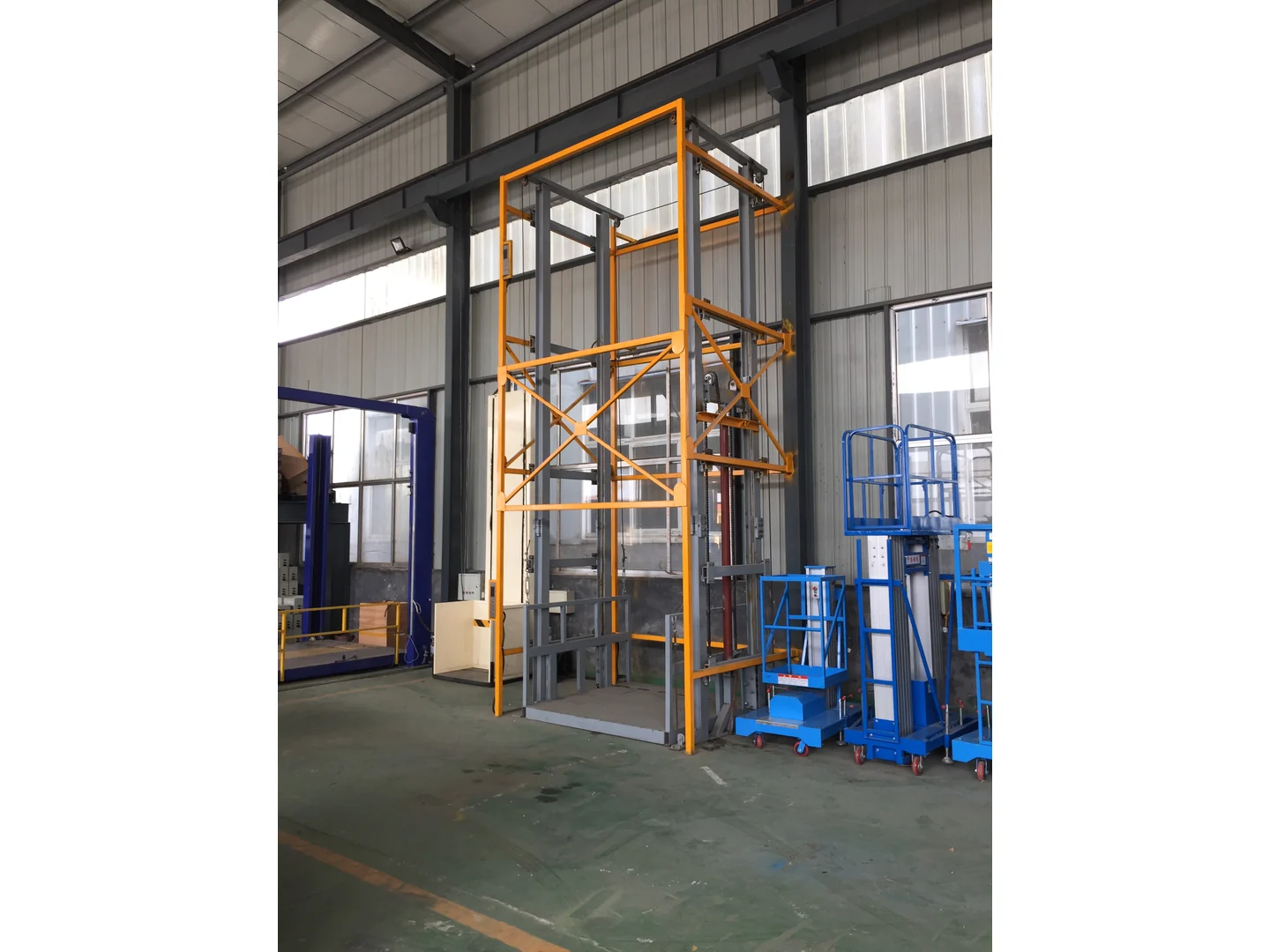 Complete gray and yellow guide rail freight lift structure beside other equipment