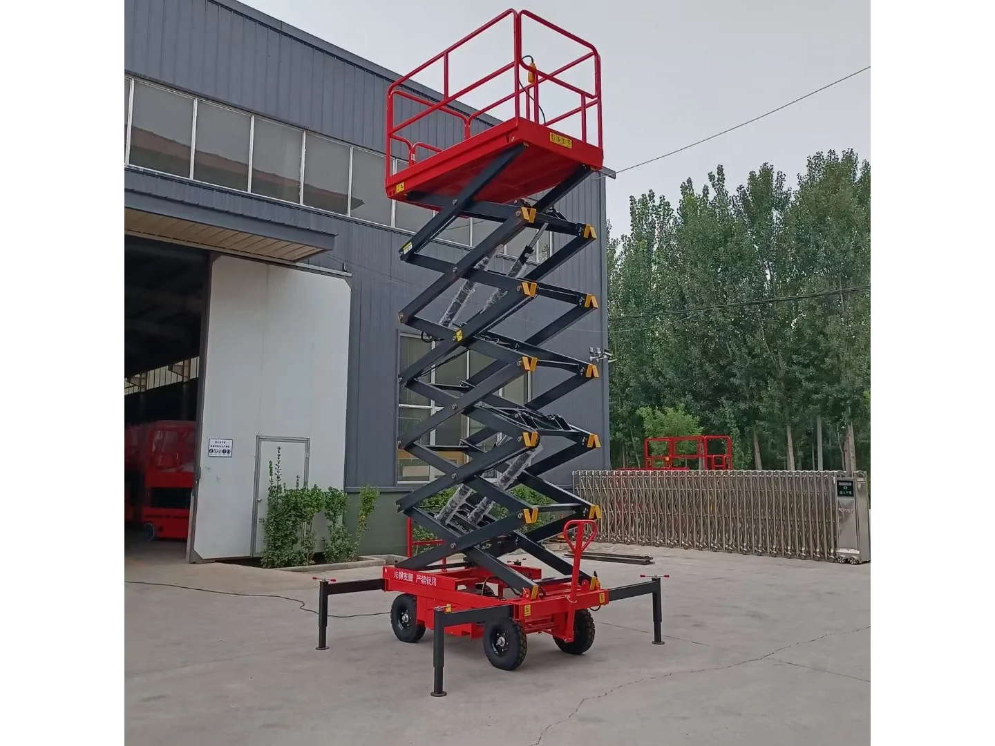Complete red mobile scissor lift raised with its platform, wheels and stabilizers visible