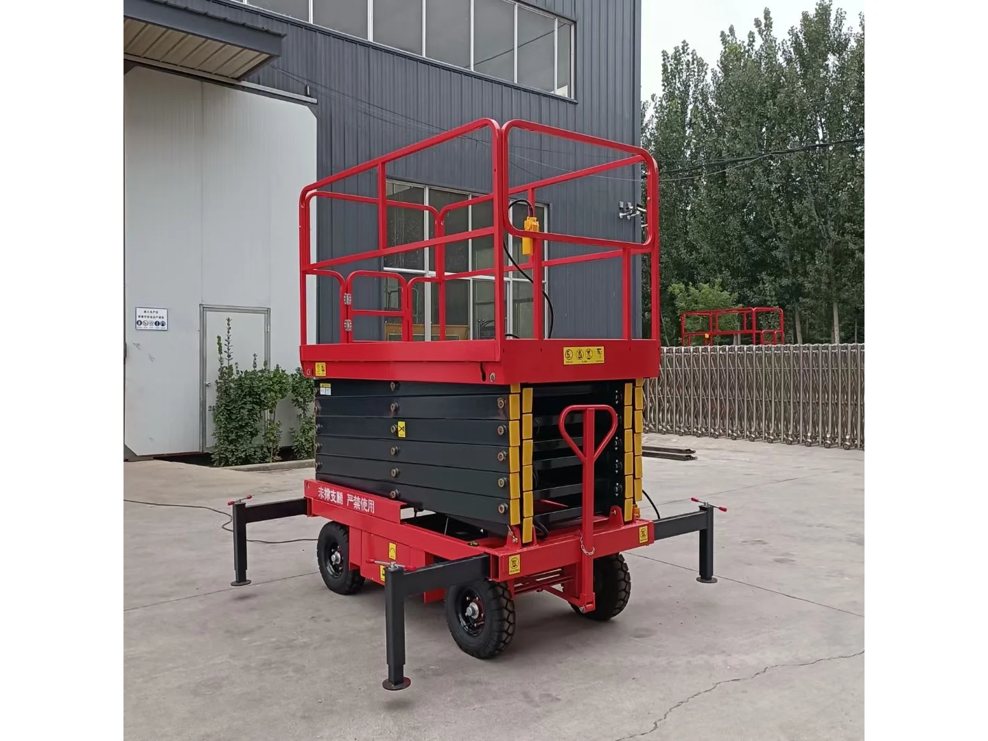 Complete red mobile scissor lift folded with its wheels and stabilizers visible outside a building