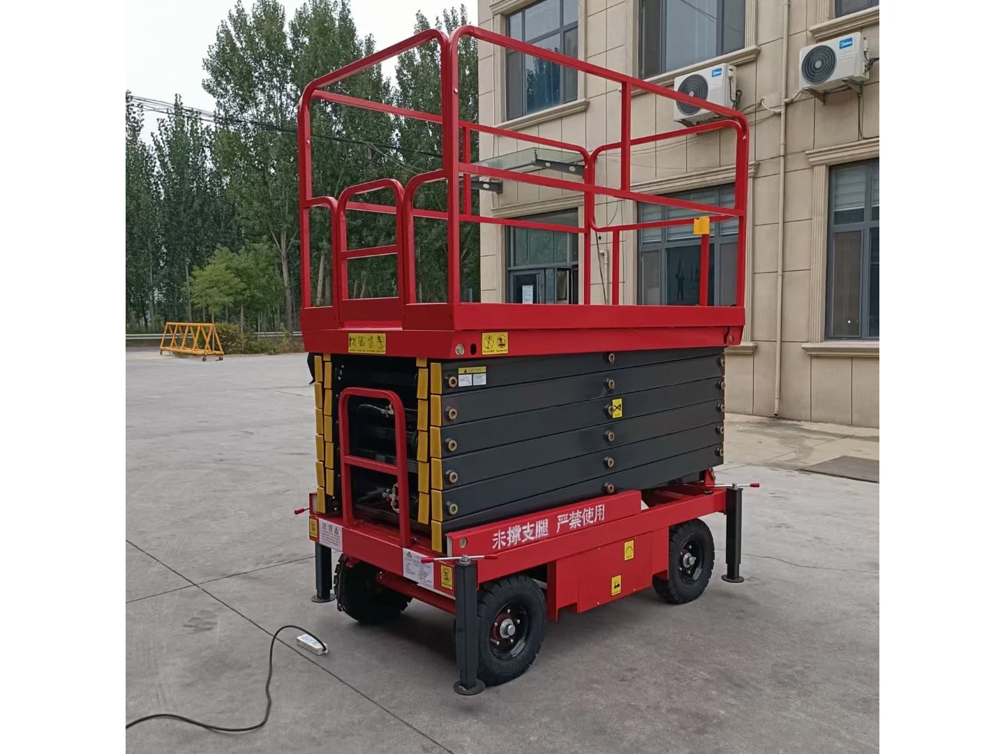 Complete red mobile scissor lift in a folded side view, with its safety labels and power cable retained