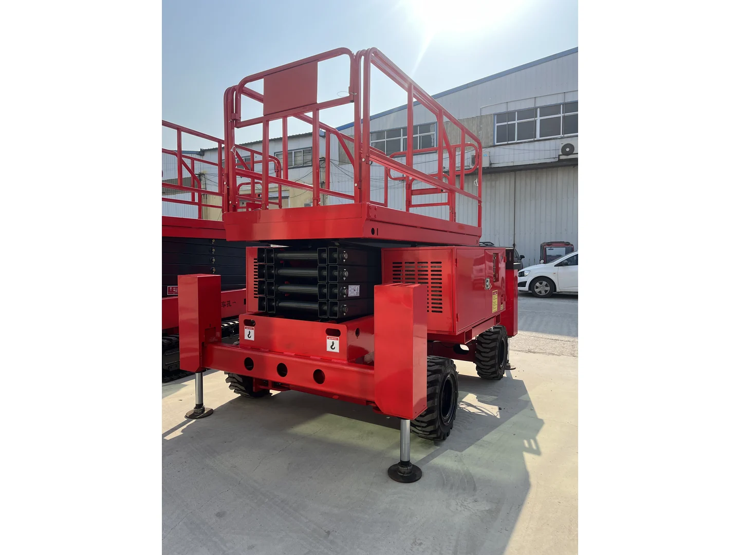 Complete red rough terrain scissor lift folded with wheels and stabilizers visible, beside other equipment