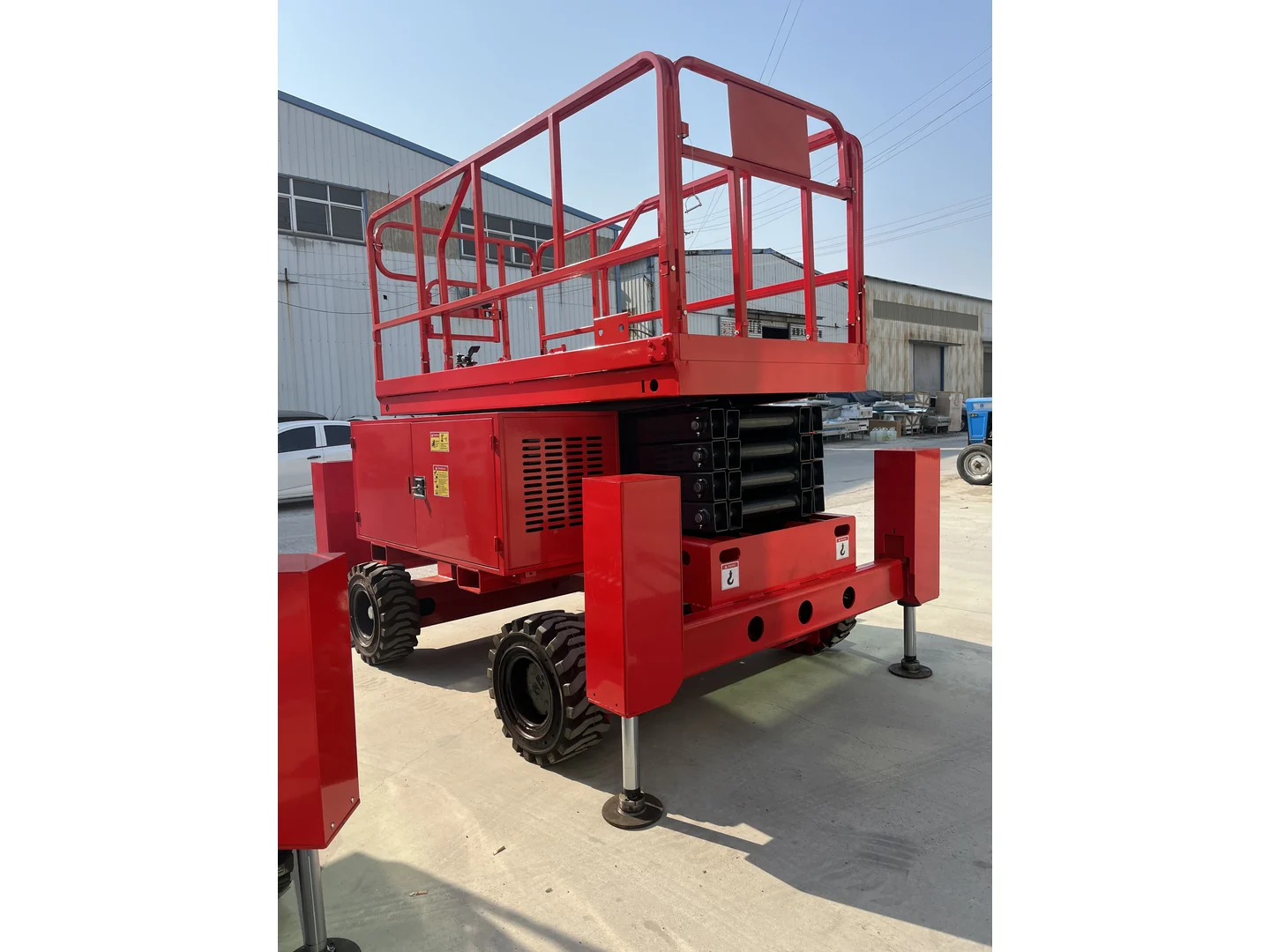 Red rough terrain scissor lift folded in an opposite three-quarter view, with its wheels and stabilizers visible