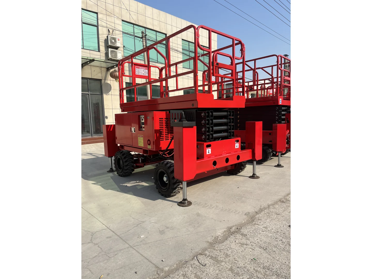 Complete red rough terrain scissor lift in a side three-quarter view beside other equipment