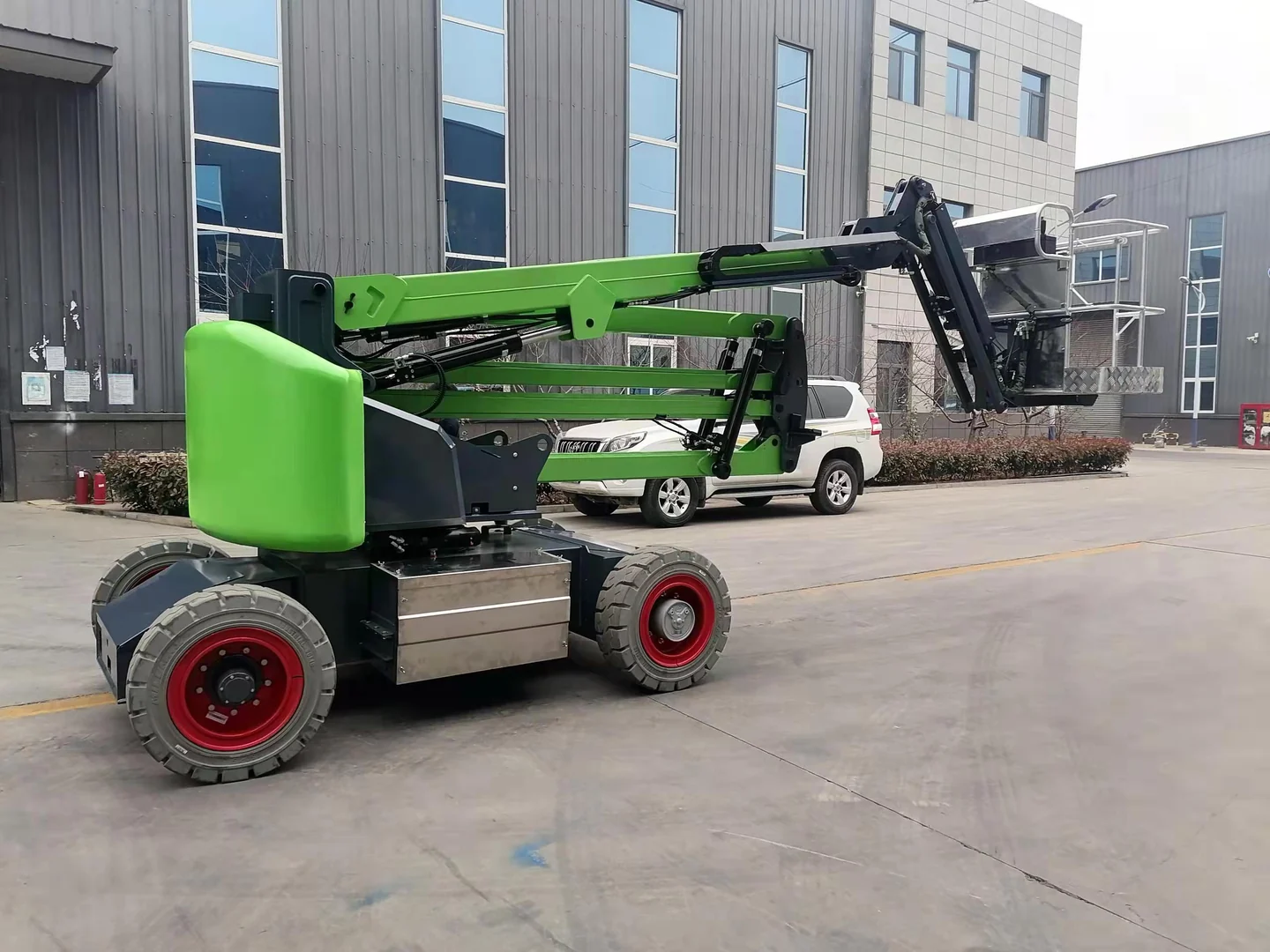 Complete green self-propelled articulating boom lift folded outside a building