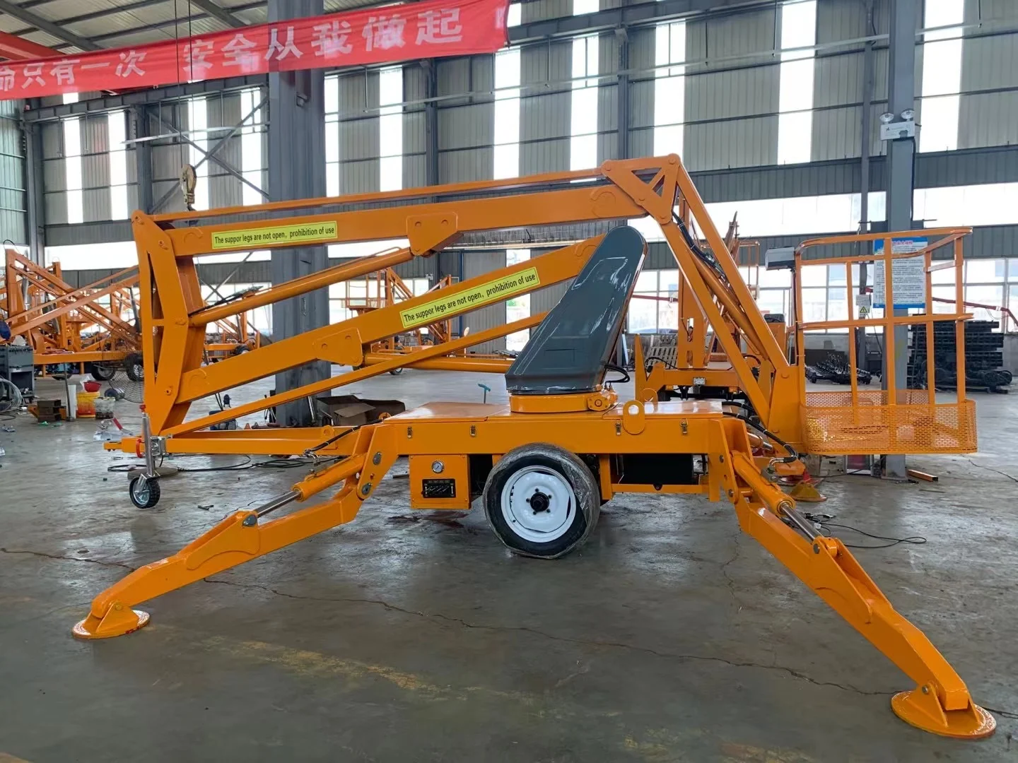 Complete orange towable articulating boom lift folded with supports deployed in a workshop