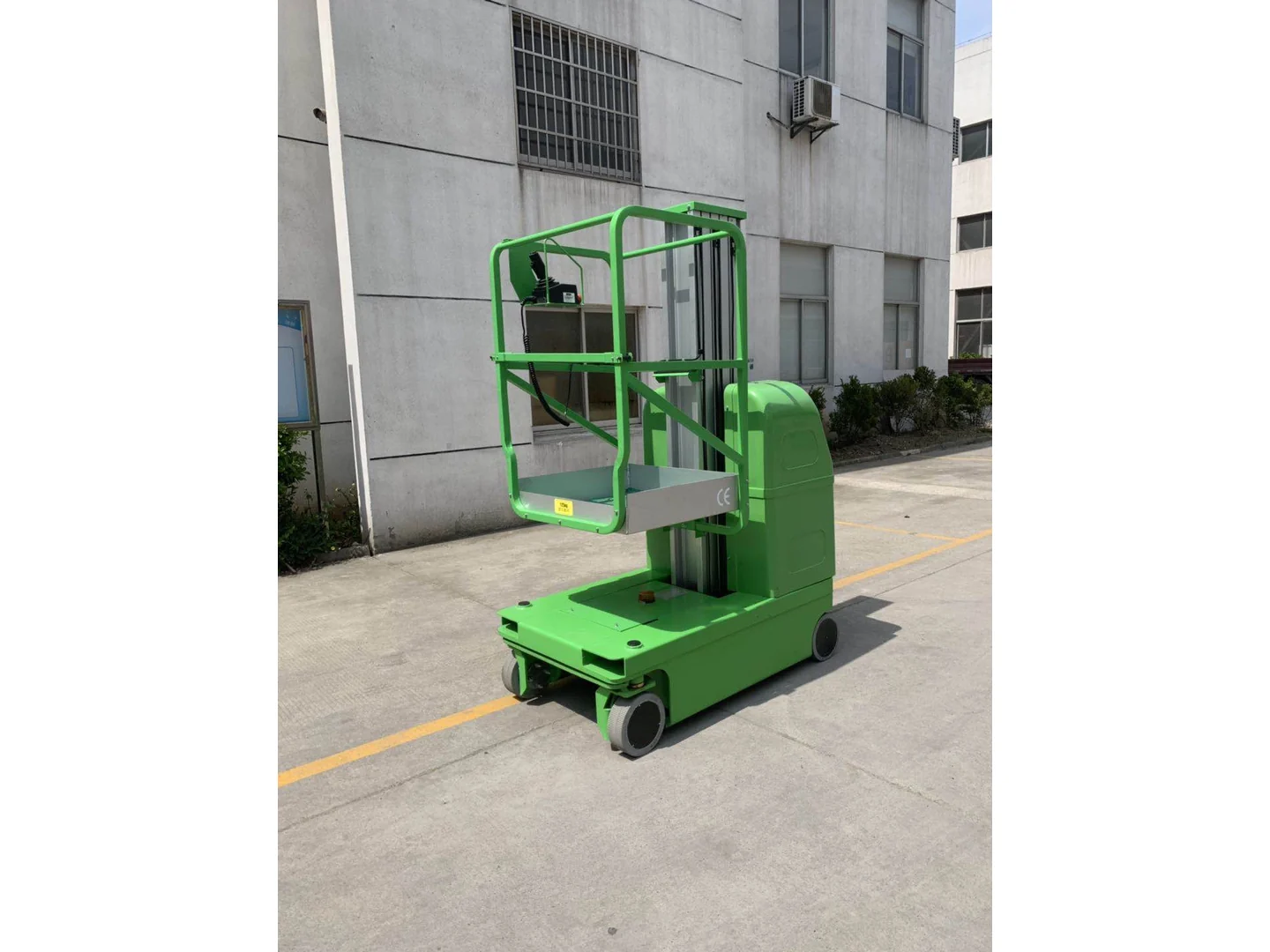 Complete green self-propelled vertical mast lift lowered outside a building